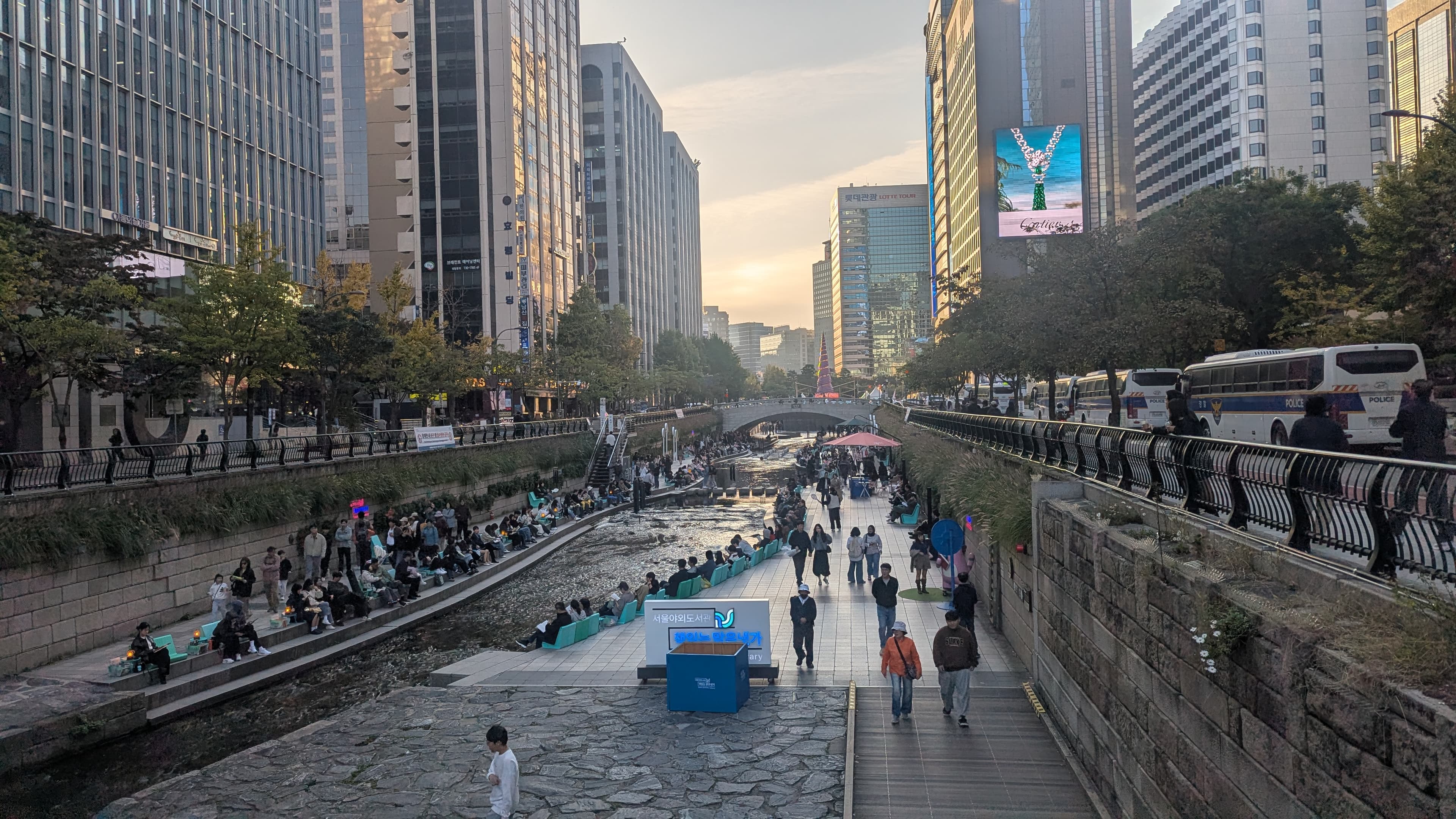 The restored Cheonggyecheon stream in central Seoul — people sitting along the daylit waterway with the Seoul Outdoor Library beside it.