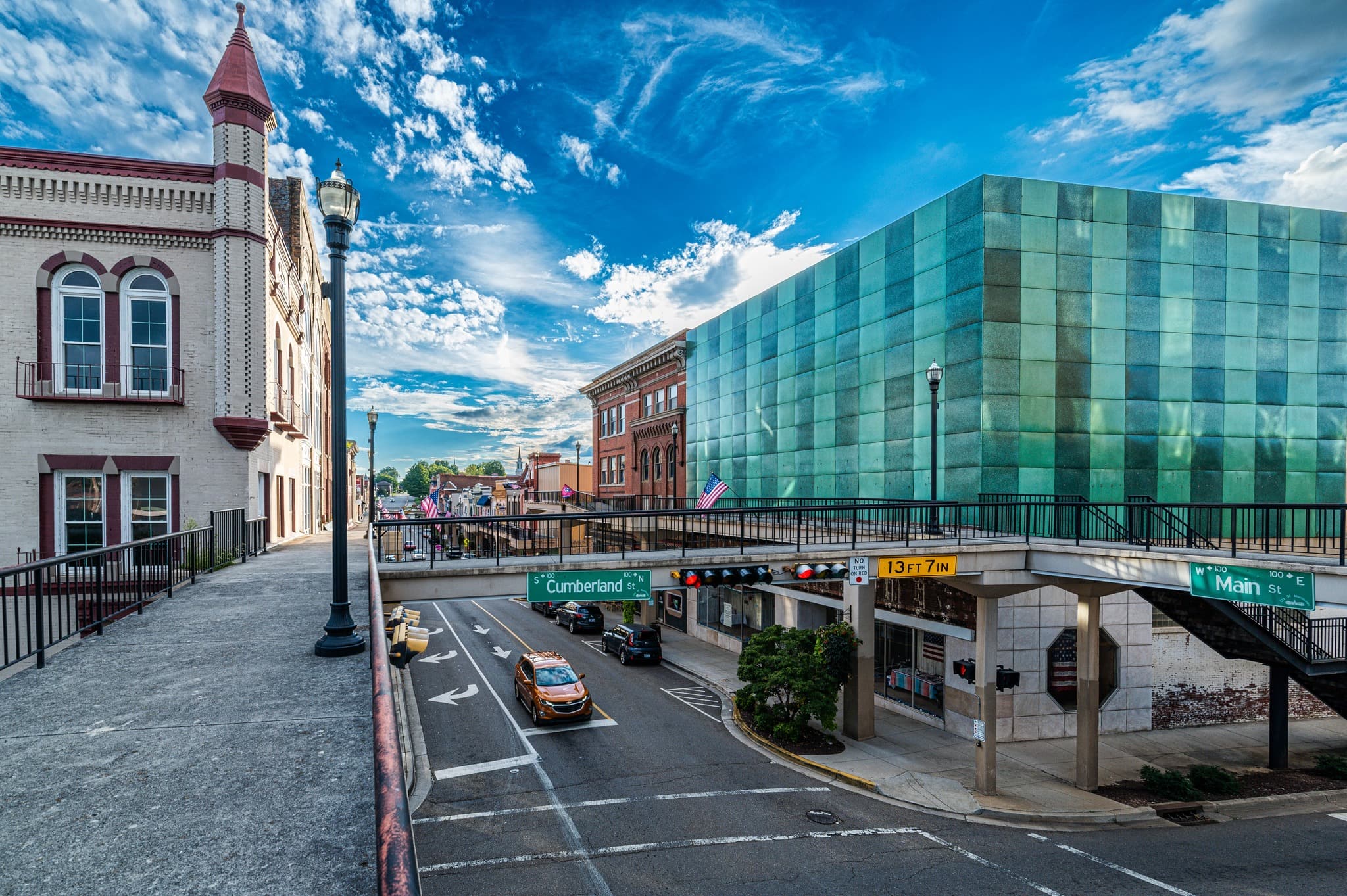 The intersection of Cumberland Street and Main Street in Morristown — the green-glazed Hamblen County complex on the right, the SkyMart elevated walkway crossing the foreground, a vintage castellated facade on the left.