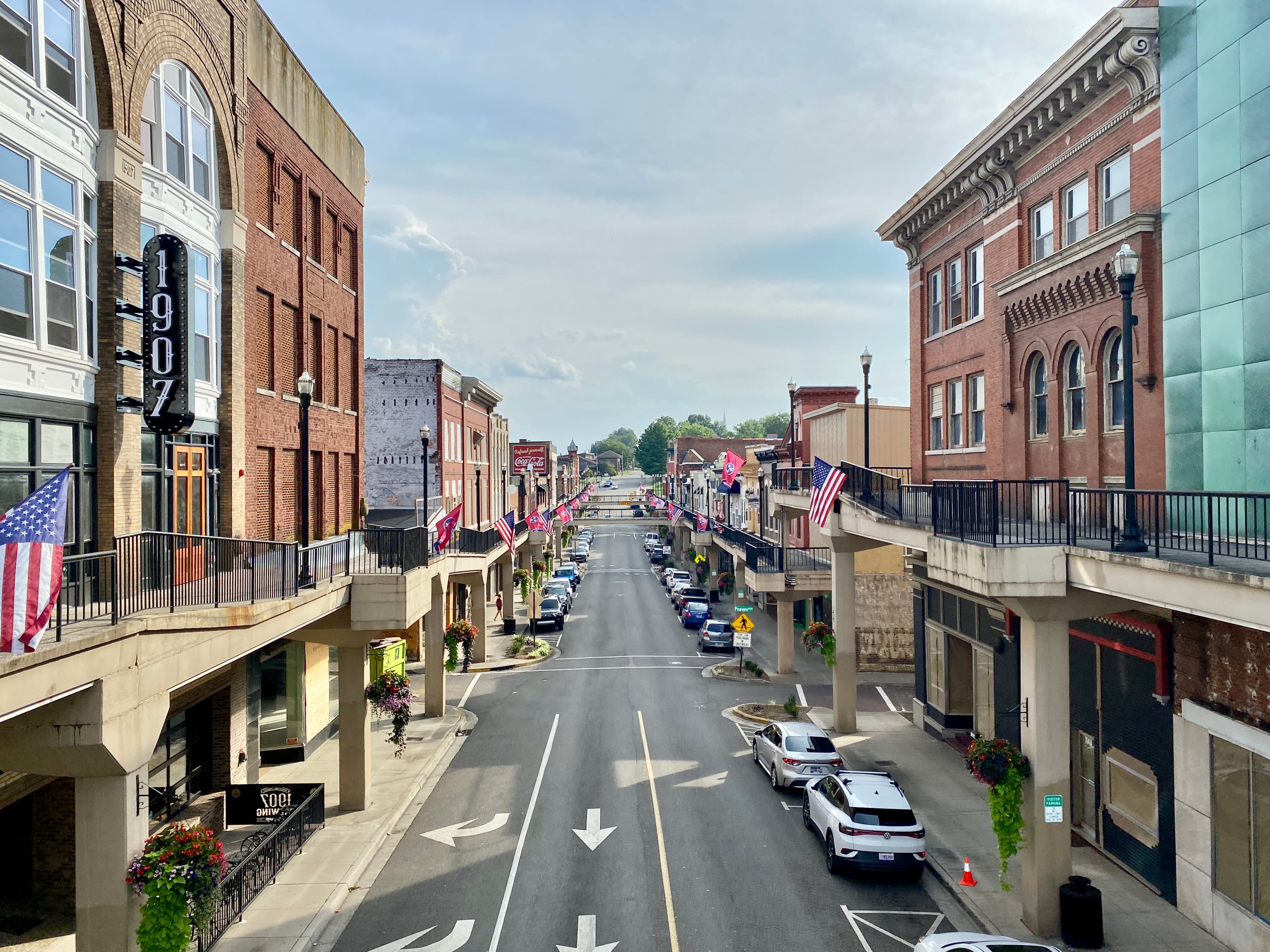Morristown, Tennessee — looking down Main Street between two raised brick storefronts, the elevated SkyMart walkways running on both sides at second-story level, hung with American and Tennessee flags.